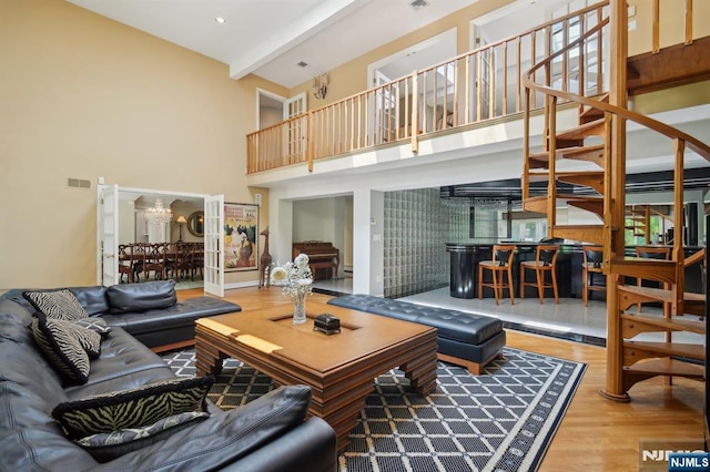 living area with wood finished floors, an inviting chandelier, stairway, visible vents, and a towering ceiling