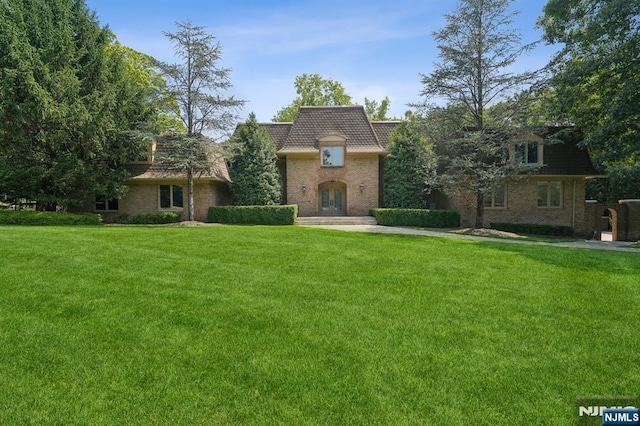 view of front of home with brick siding, french doors, a front yard, and mansard roof