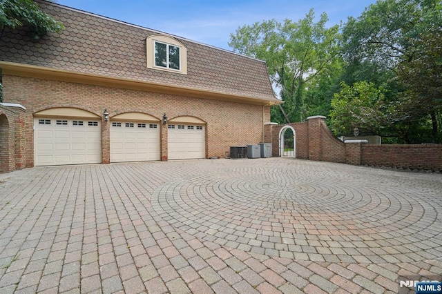 exterior space with a gate, brick siding, curved driveway, and mansard roof