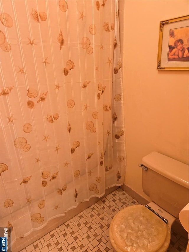 bathroom with toilet, a shower with shower curtain, and baseboards