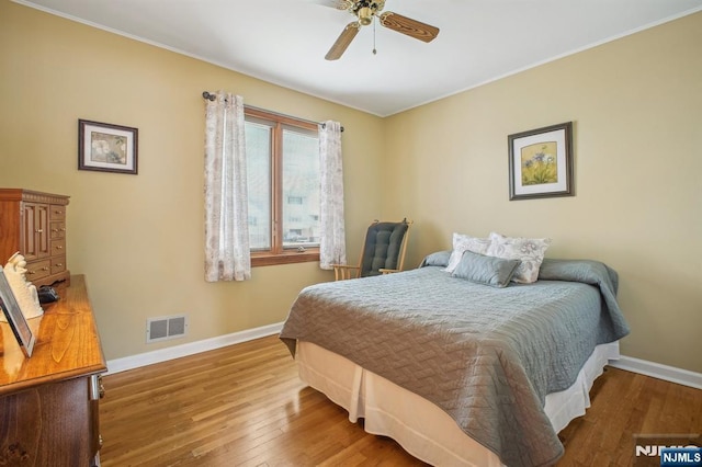 bedroom featuring baseboards, visible vents, hardwood / wood-style flooring, and ornamental molding