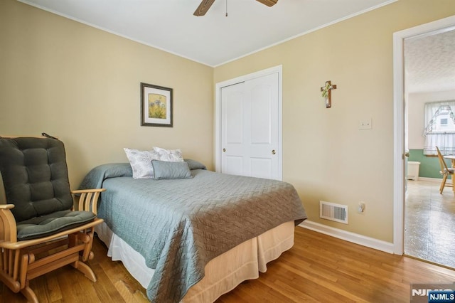 bedroom featuring wood finished floors, baseboards, visible vents, a ceiling fan, and crown molding