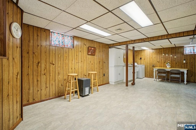 basement with tile patterned floors, washer / dryer, a paneled ceiling, and wood walls