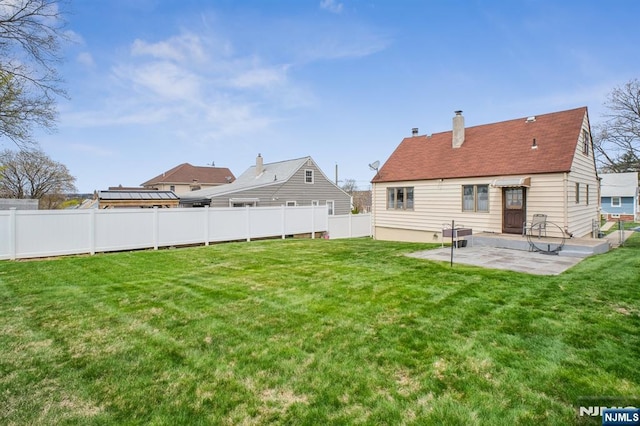 back of house with a lawn, a chimney, a fenced backyard, and a patio area