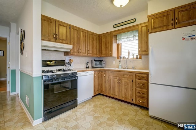 kitchen with tasteful backsplash, white appliances, under cabinet range hood, light countertops, and a sink