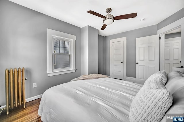 bedroom featuring a closet, ceiling fan, radiator heating unit, baseboards, and wood finished floors