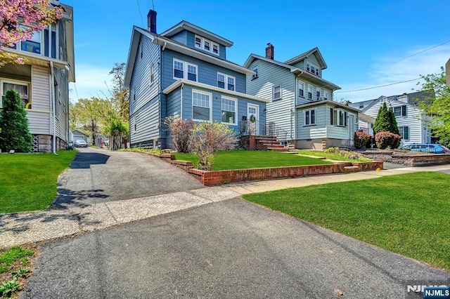 traditional style home featuring a chimney, aphalt driveway, and a front yard