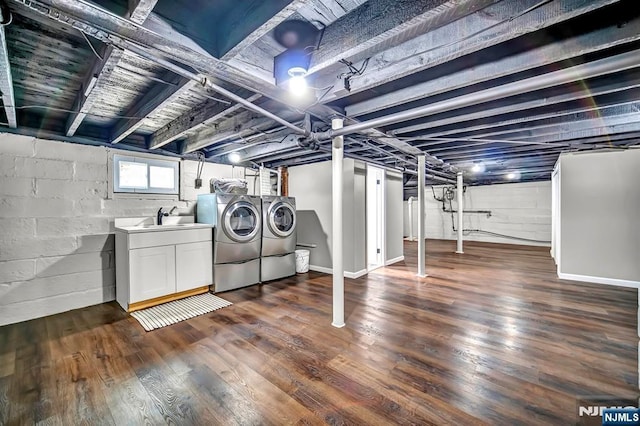 basement with dark wood finished floors, baseboards, concrete block wall, and washer and clothes dryer