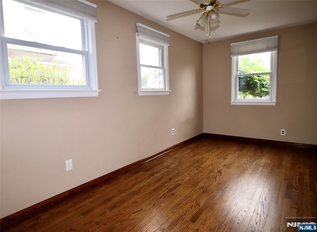 spare room featuring baseboards, ceiling fan, and dark wood-type flooring