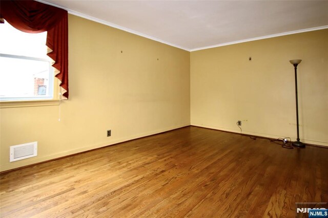 spare room with baseboards, visible vents, wood finished floors, and crown molding