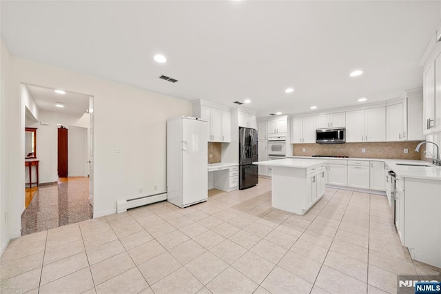 kitchen with visible vents, a sink, a baseboard radiator, stainless steel microwave, and freestanding refrigerator