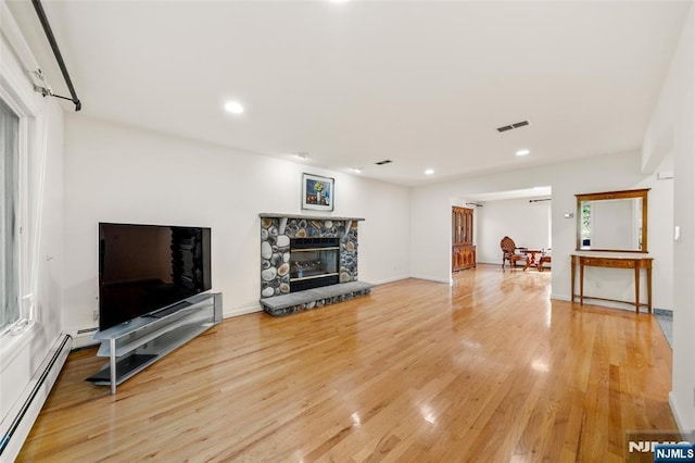 living area featuring a stone fireplace, visible vents, wood finished floors, a baseboard heating unit, and recessed lighting