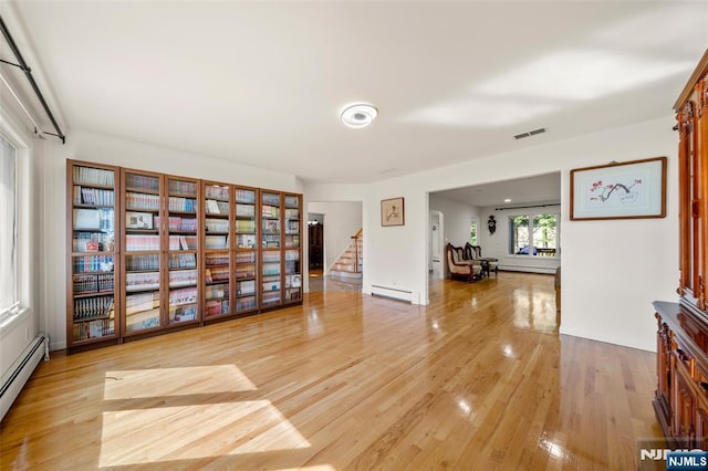interior space with stairs, a baseboard heating unit, visible vents, and light wood-style flooring