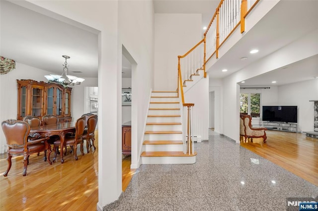 stairway featuring baseboards, an inviting chandelier, granite finish floor, and a towering ceiling