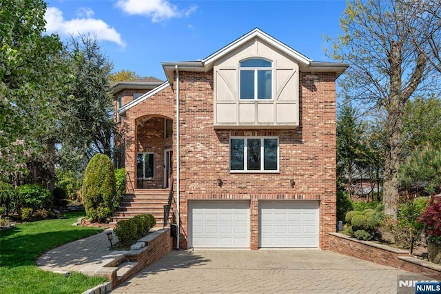tudor-style house with brick siding, decorative driveway, a front yard, and a garage