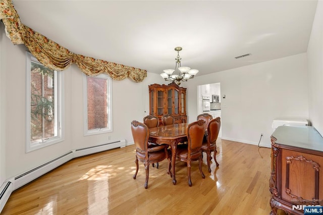 dining space featuring visible vents, baseboards, a baseboard heating unit, light wood finished floors, and a chandelier