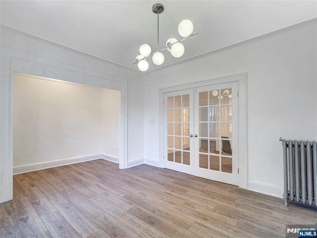 unfurnished dining area featuring french doors, baseboards, an inviting chandelier, radiator, and wood finished floors