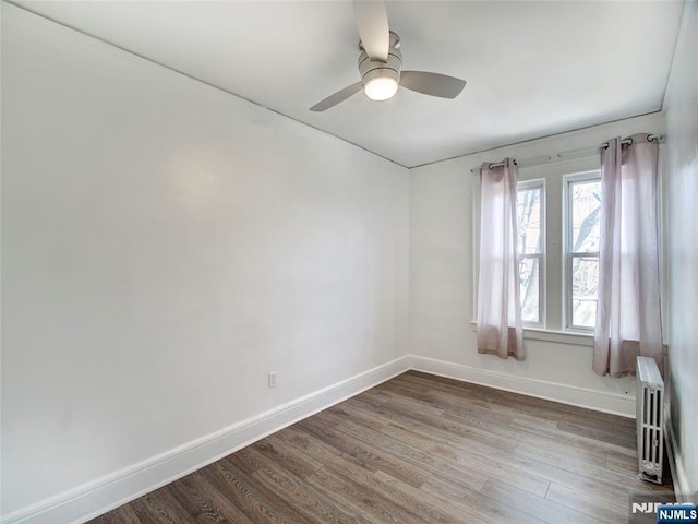 spare room featuring ceiling fan, radiator heating unit, wood finished floors, and baseboards
