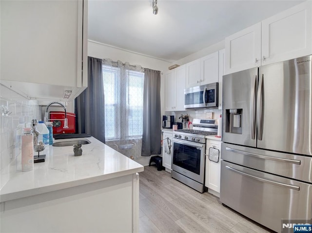 kitchen with white cabinetry, decorative backsplash, a sink, light wood-style floors, and stainless steel appliances