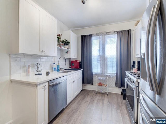 kitchen with white cabinetry, light wood-style flooring, a sink, appliances with stainless steel finishes, and backsplash