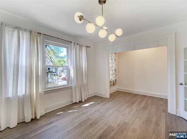 unfurnished room with an inviting chandelier, baseboards, and light wood-style floors