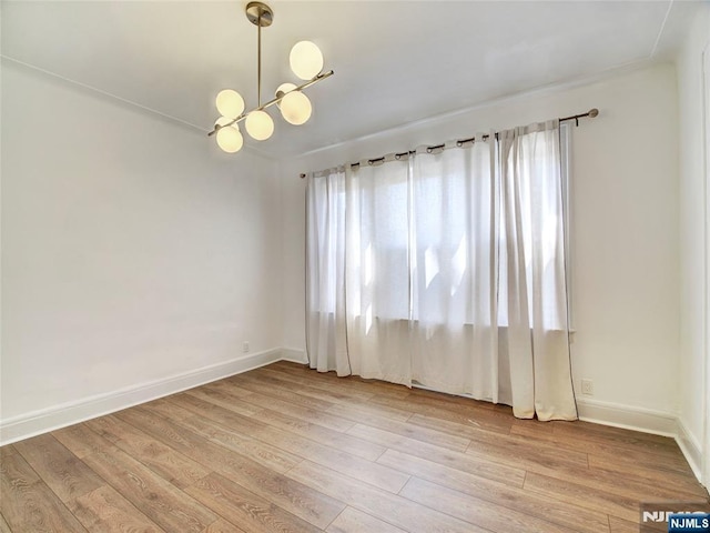 spare room featuring a notable chandelier, baseboards, light wood-style flooring, and a healthy amount of sunlight