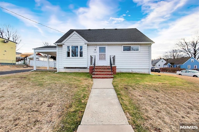 bungalow featuring a front yard, a shingled roof, and an attached carport