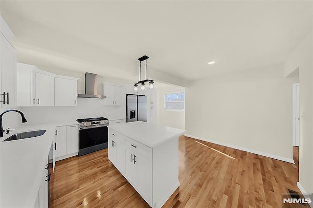 kitchen with stainless steel appliances, a kitchen island, wall chimney range hood, light wood finished floors, and a sink