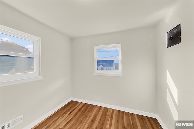 unfurnished room featuring baseboards, visible vents, wood finished floors, and plenty of natural light