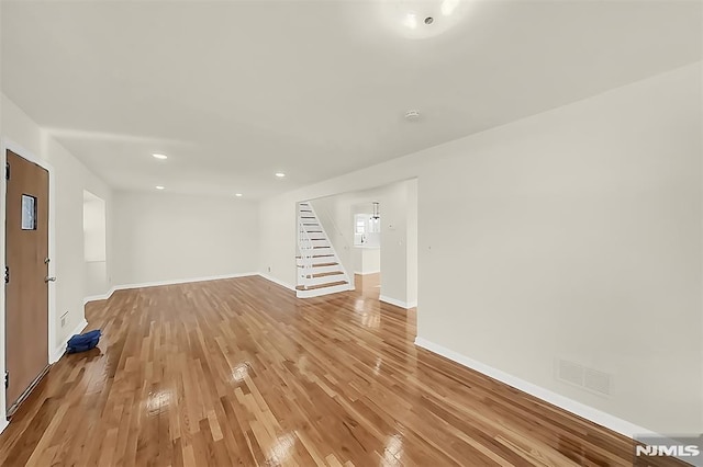 unfurnished living room with light wood-style flooring, visible vents, baseboards, recessed lighting, and stairs