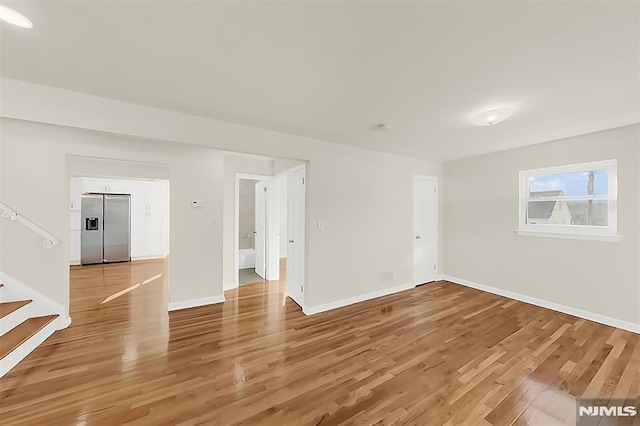 spare room with light wood finished floors, stairs, and baseboards
