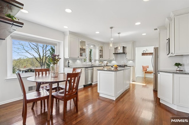 kitchen featuring decorative backsplash, a kitchen island, wall chimney range hood, white cabinets, and appliances with stainless steel finishes