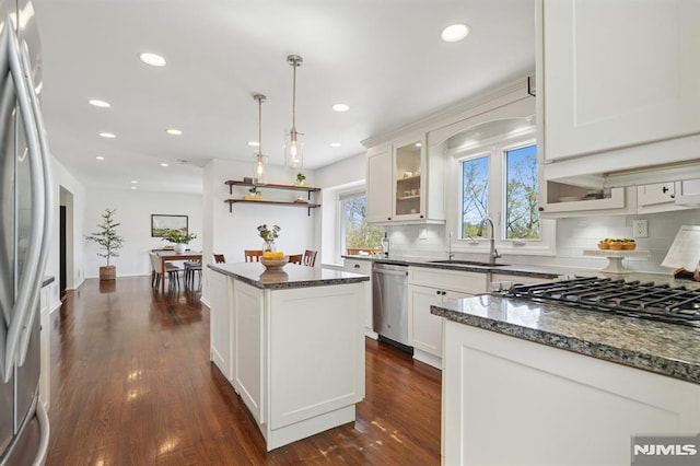 kitchen with dark stone countertops, appliances with stainless steel finishes, backsplash, a sink, and dark wood-style floors
