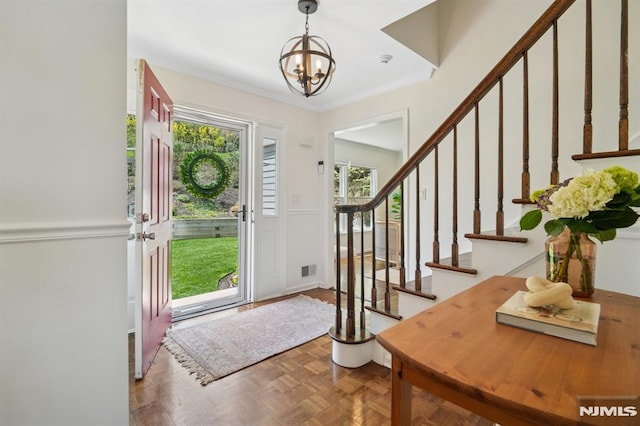 entrance foyer featuring ornamental molding, a notable chandelier, stairway, and visible vents
