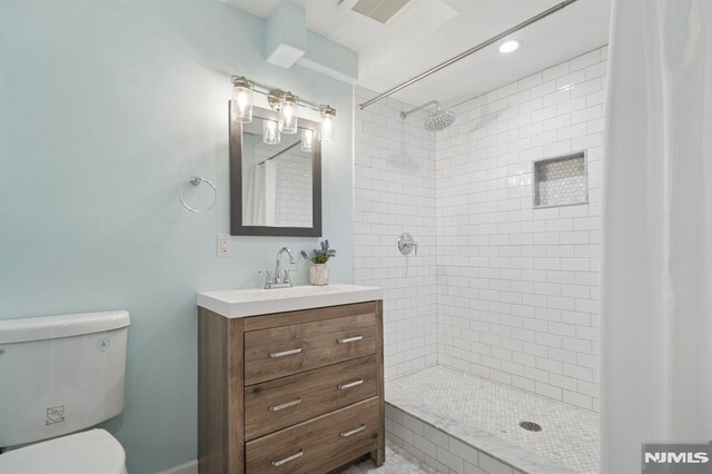 full bathroom with visible vents, toilet, a tile shower, and vanity