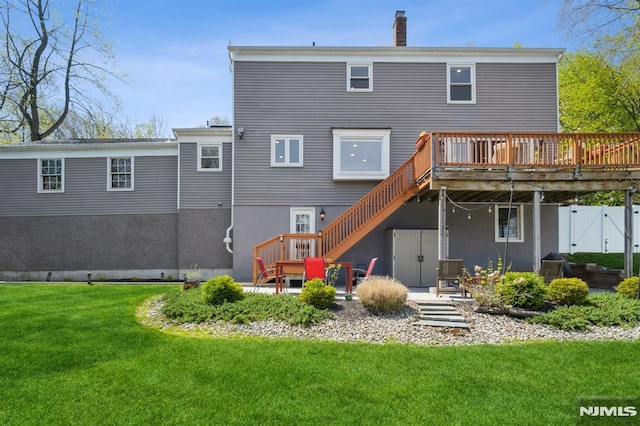 rear view of house featuring a deck, a chimney, a yard, stairway, and fence