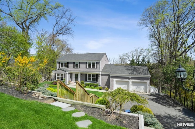 colonial home featuring driveway, fence, a front yard, and a garage