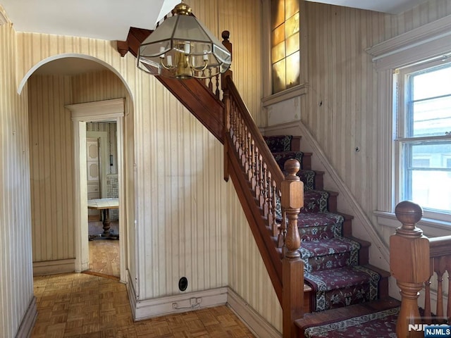 staircase with baseboards, wallpapered walls, arched walkways, and a notable chandelier