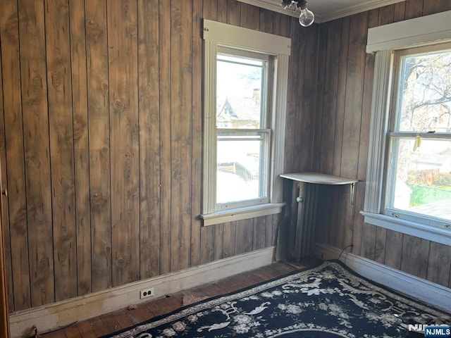 unfurnished room with wooden walls, ornamental molding, wood finished floors, and plenty of natural light