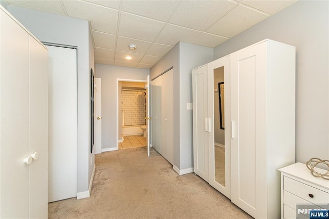 hall featuring baseboards, a drop ceiling, and light carpet