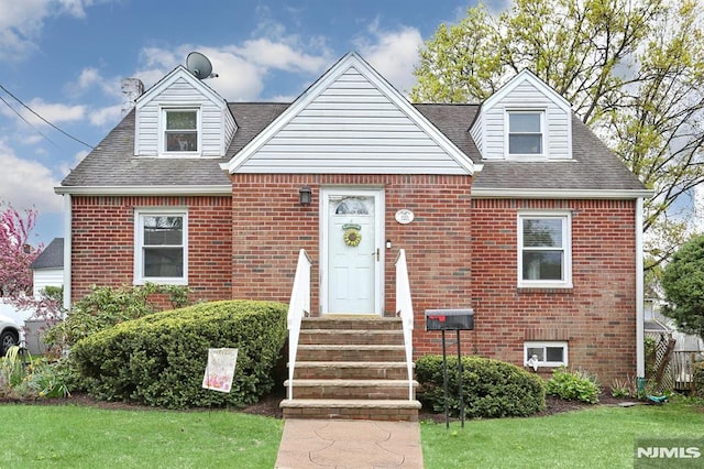 new england style home with brick siding, roof with shingles, a front yard, and entry steps