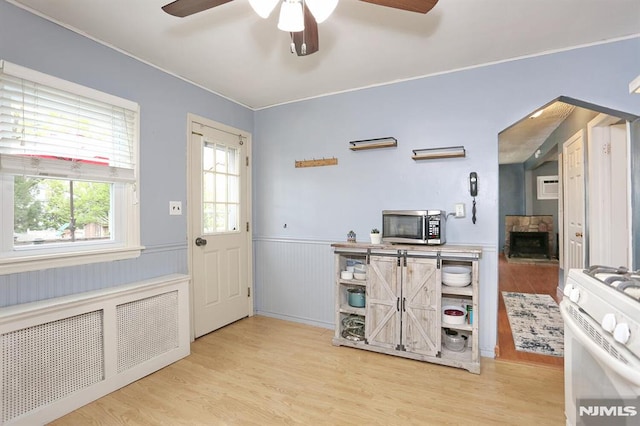 kitchen with wainscoting, radiator, gas range gas stove, ceiling fan, and stainless steel microwave