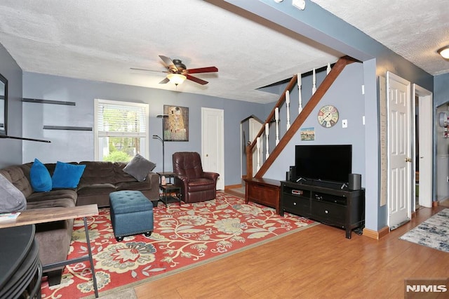 living room featuring ceiling fan, a textured ceiling, baseboards, wood finished floors, and stairway
