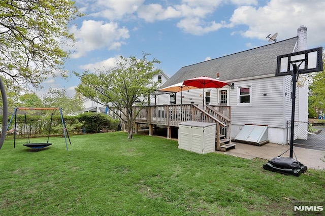 rear view of property featuring a deck, a chimney, a shingled roof, a playground, and a yard