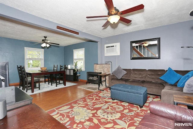 living area featuring ceiling fan, a textured ceiling, a wood stove, wood finished floors, and an AC wall unit