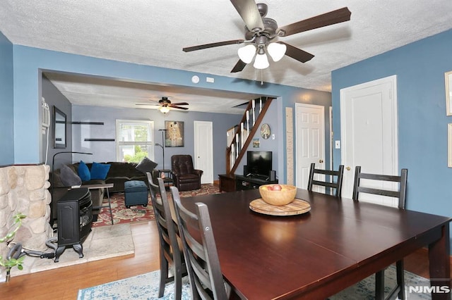 dining space with a wood stove, wood finished floors, stairway, a textured ceiling, and a ceiling fan