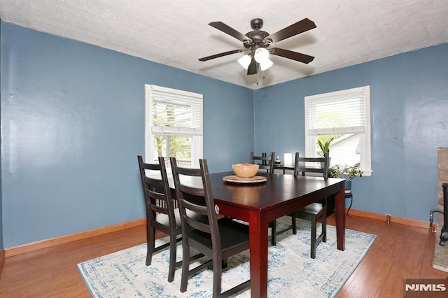 dining area featuring baseboards, a ceiling fan, a textured ceiling, and wood finished floors