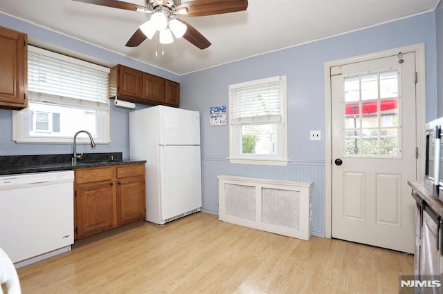 kitchen featuring brown cabinets, wainscoting, a sink, white appliances, and light wood-type flooring