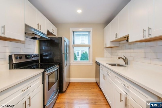 kitchen featuring stainless steel appliances, light wood-style floors, under cabinet range hood, a sink, and baseboards