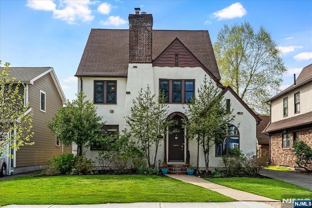 view of front facade with a chimney, a front lawn, a shingled roof, entry steps, and stucco siding
